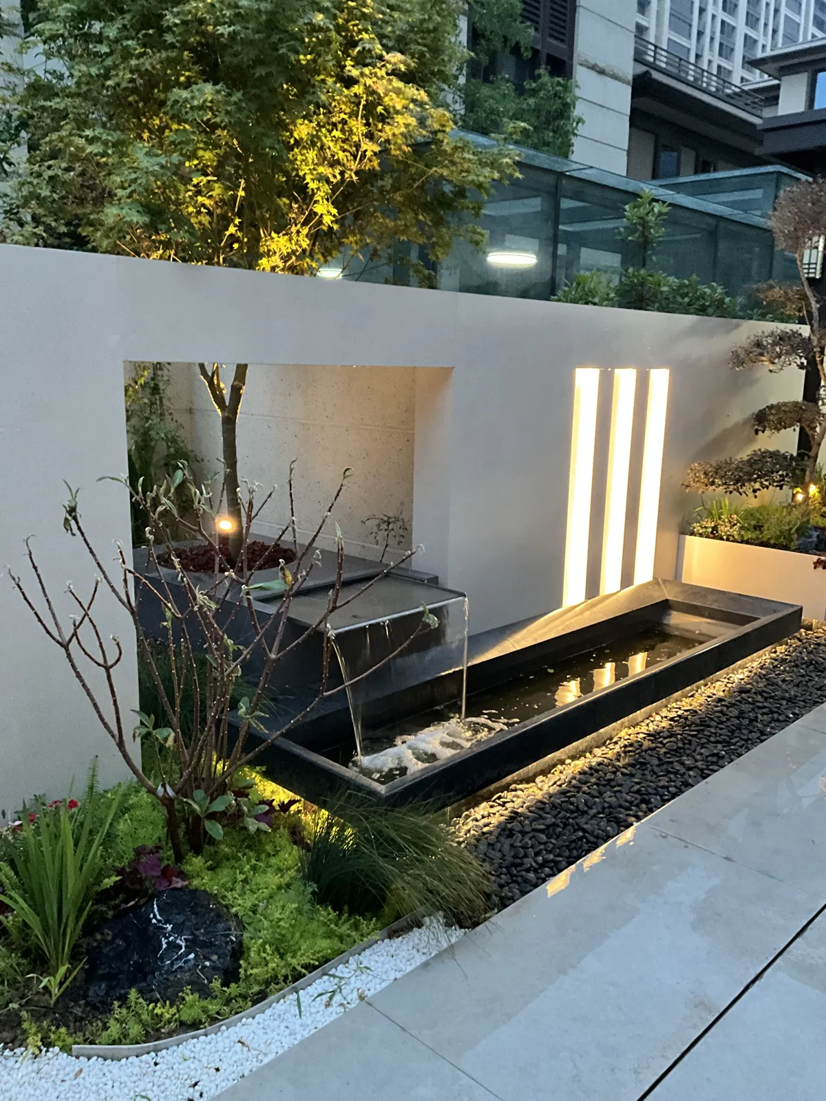 郑州兰乔圣菲完工实景:景墙开洞与跌水,植物从开口后露出,墙脚保留水池与卵石。