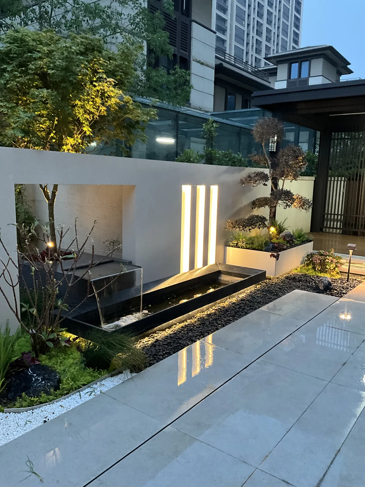 郑州兰乔圣菲完工实景:浅色景墙、三道竖向灯带与深色水池形成清楚的明暗关系。