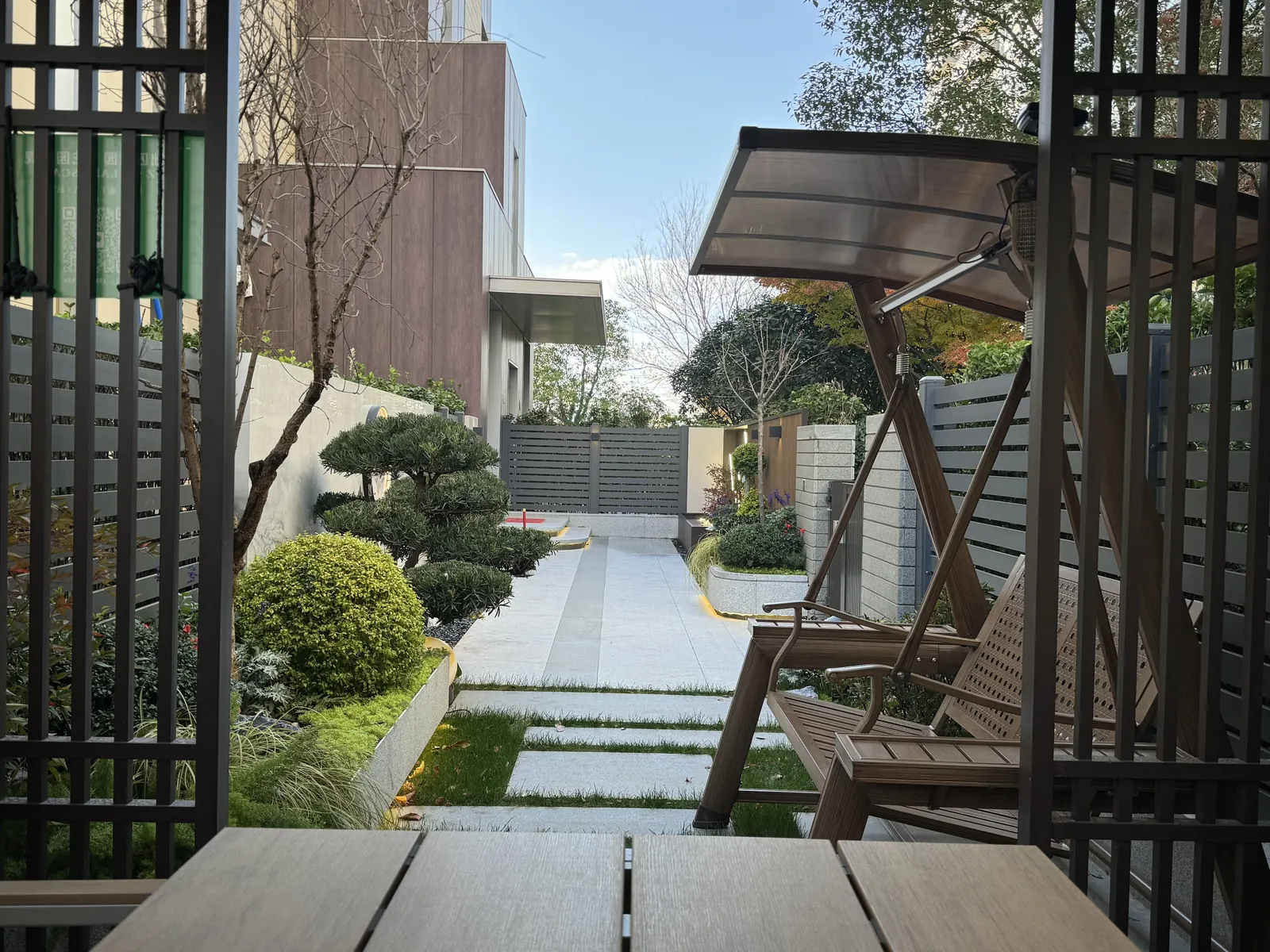 永威上和郡完工实景：休闲区视角：从廊架内看秋千、植物池与通往入口的铺装。