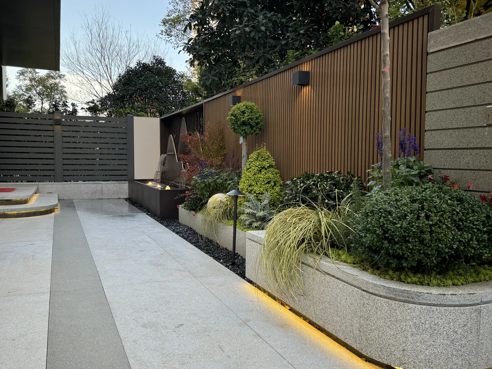 永威上和郡完工实景：入户花境：木色格栅为背景，弧形花池与水景沿通道展开。